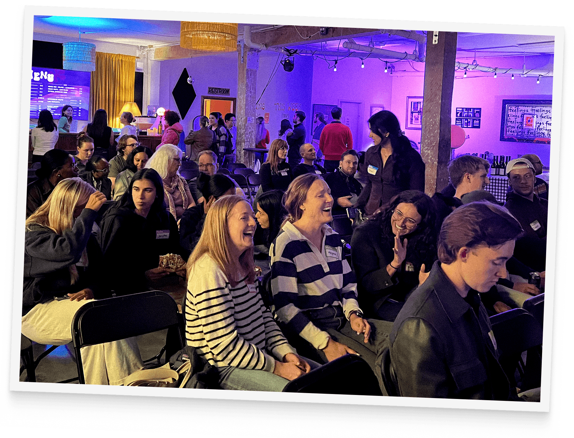 A tilted photo of a packed Big Brain audience laughing and chatting in a warmly lit bar venue