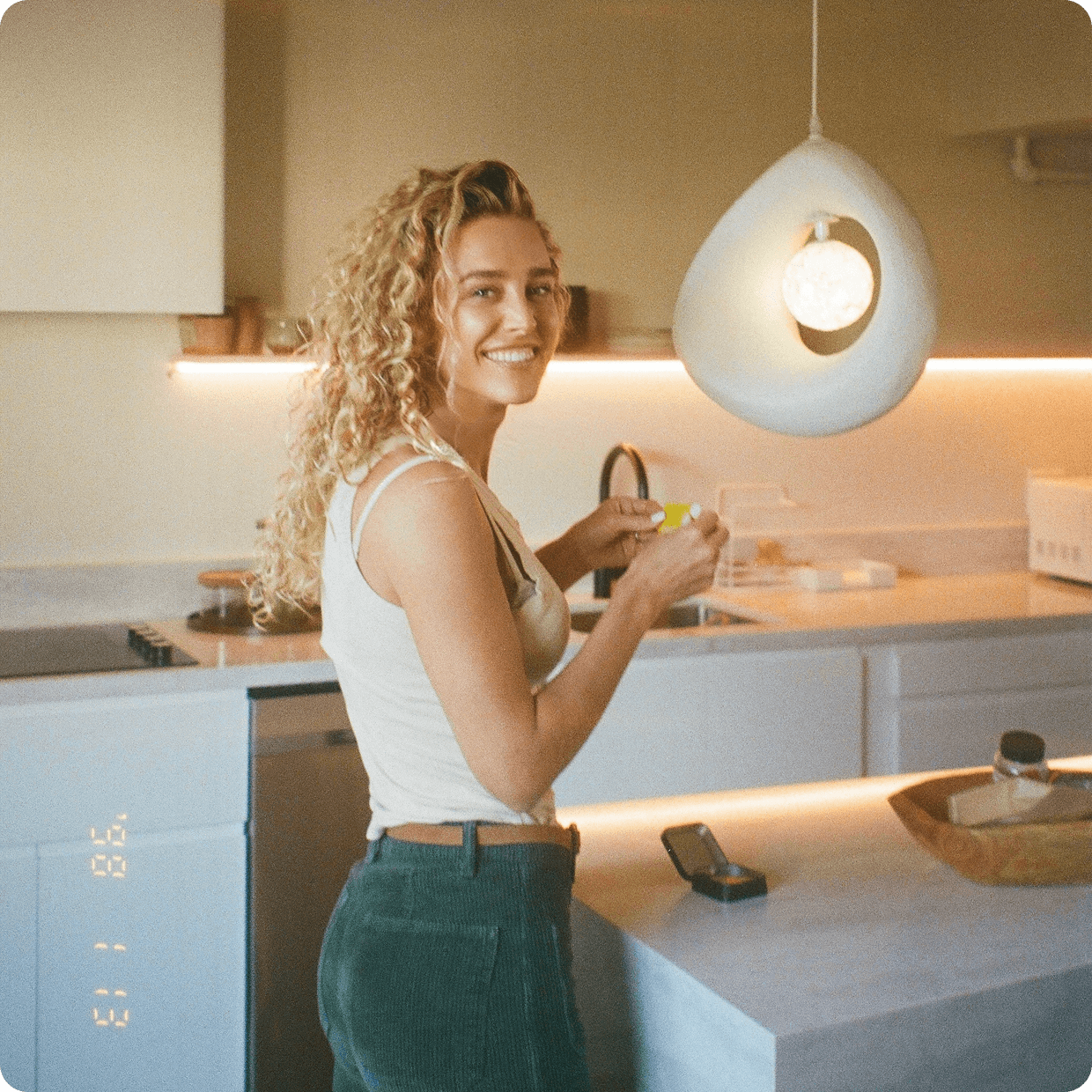 Savannah smiling in a minimalist kitchen at Moss, leaning against a marble counter under a large egg-shaped pendant lamp