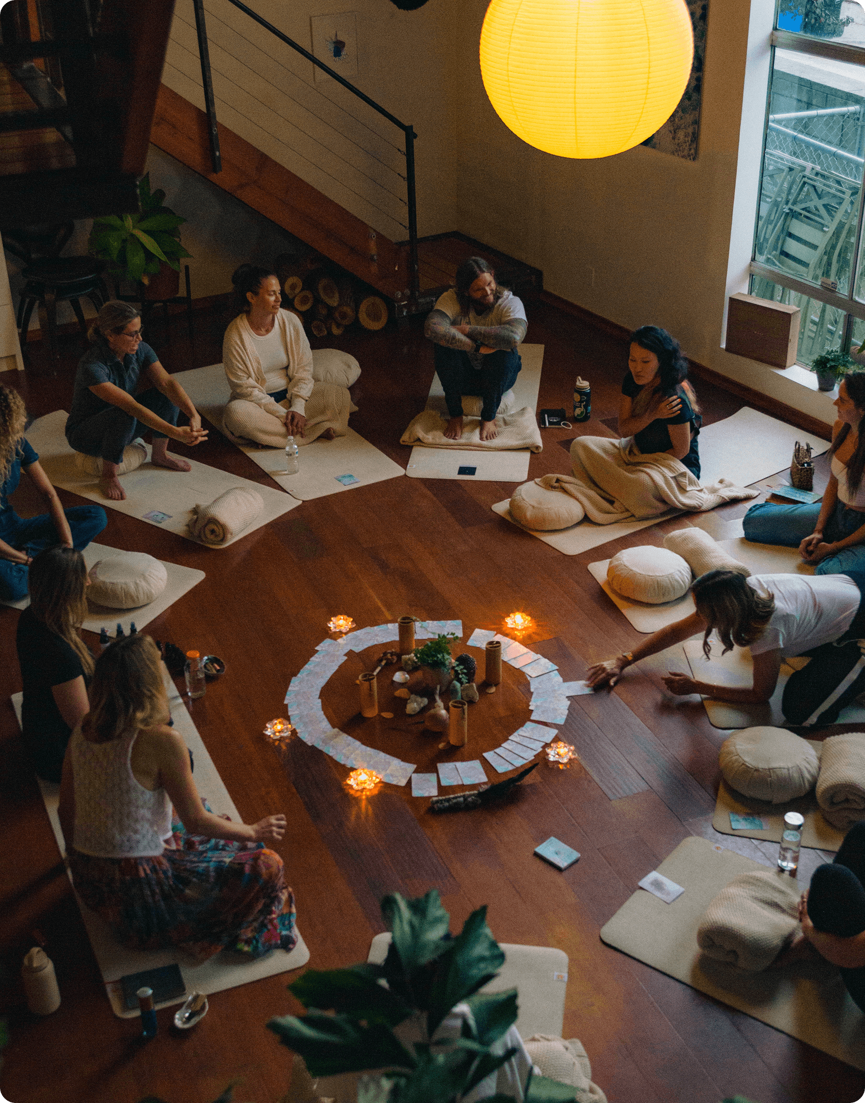 An overhead view of a meditation circle at Moss with participants seated on mats around a candlelit altar