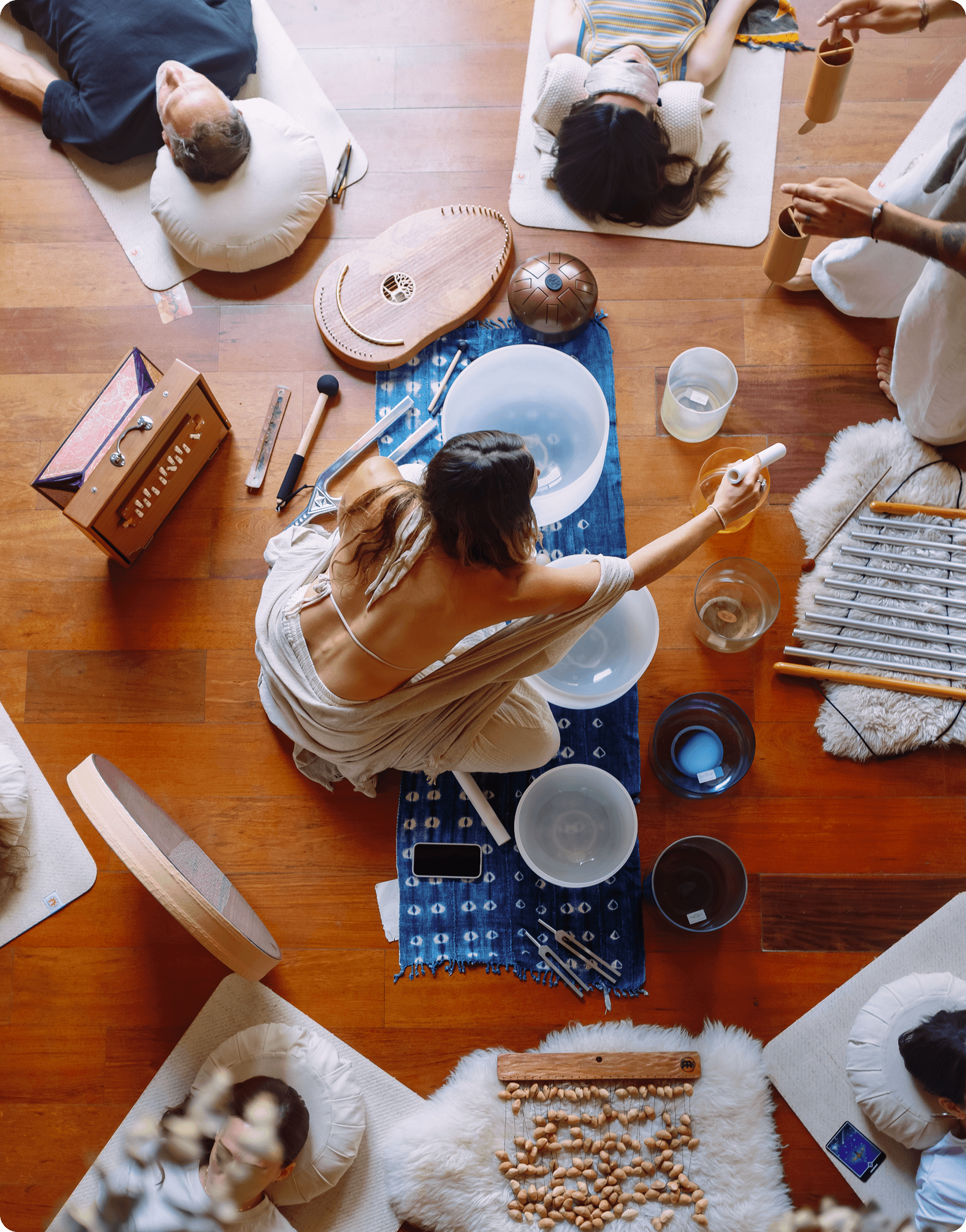 An overhead shot of a sound bath at Moss with a facilitator seated among crystal singing bowls, chimes and other instruments while participants lie around her