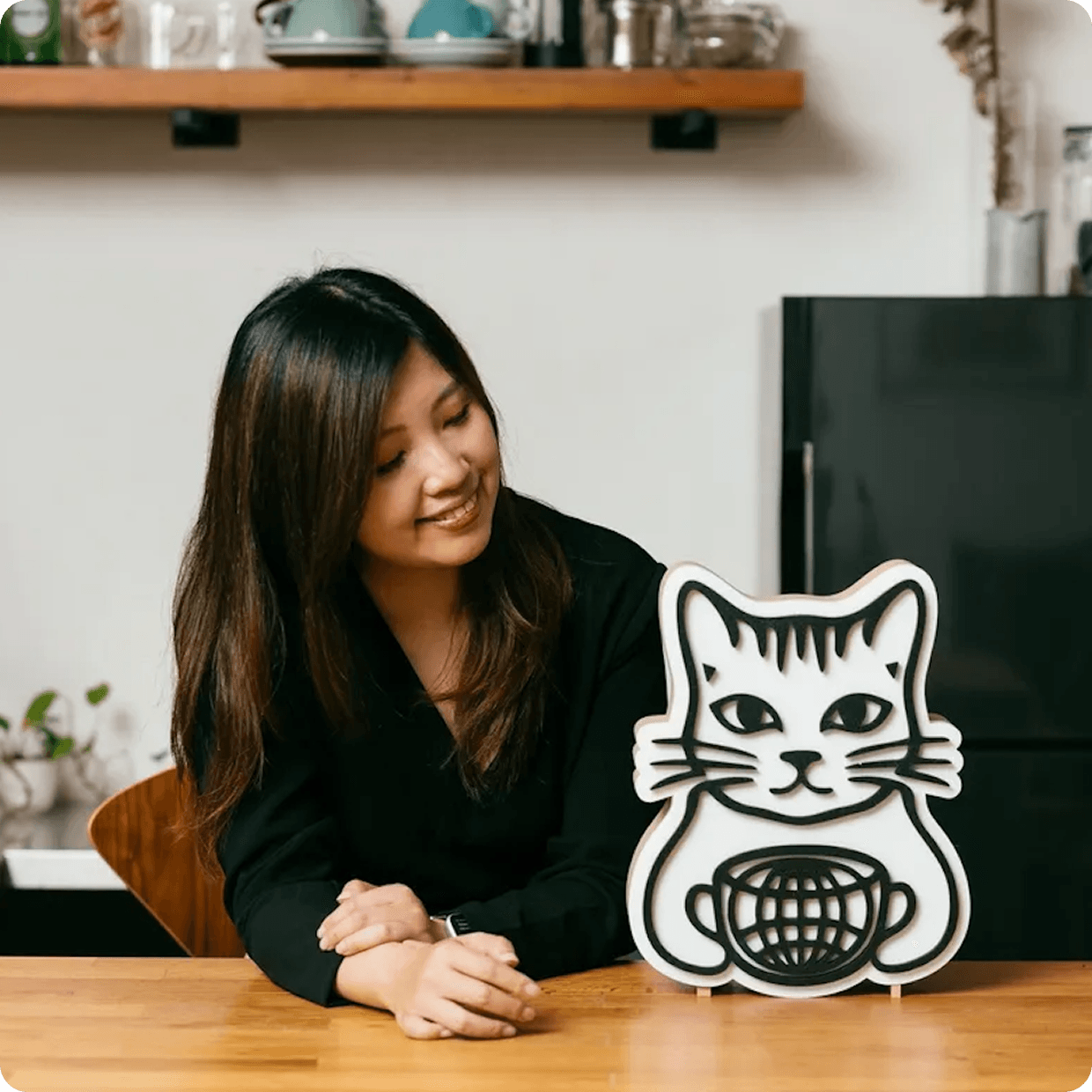 Shirley smiling at a wooden table beside a cat-shaped World Cafe CAT sign