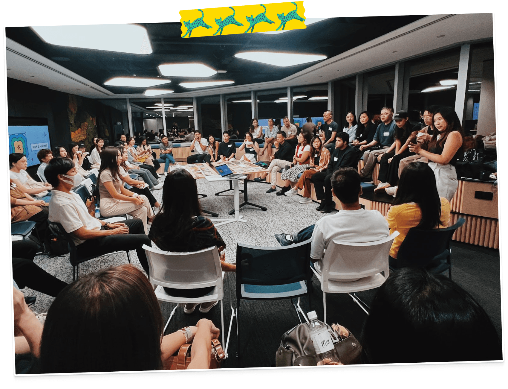 A large group of people gathered in a circle, listening to a speaker in World Cafe CAT.